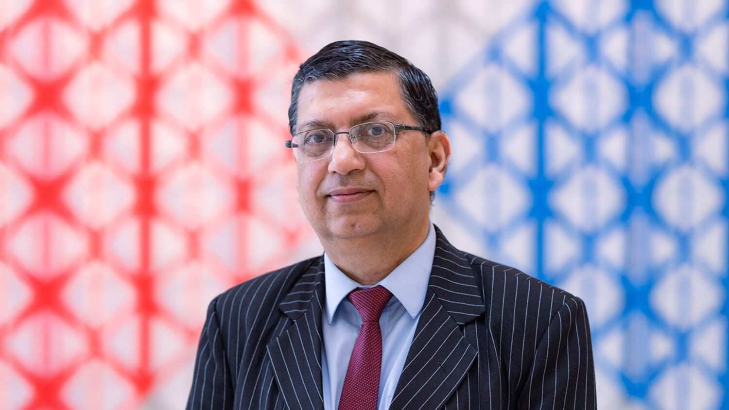 Dr Najam Abbas in a formal suit posing against a colourful background.