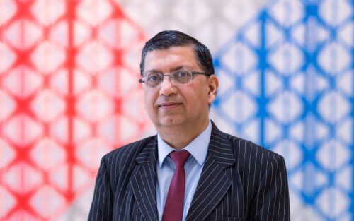 Dr Najam Abbas in a formal suit posing against a colourful background.