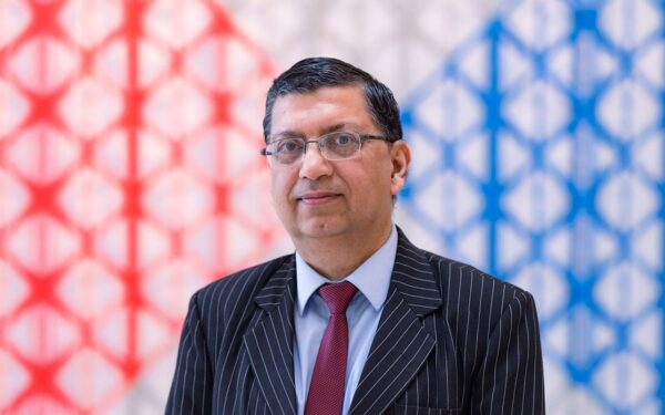 Dr Najam Abbas in a formal suit posing against a colourful background.