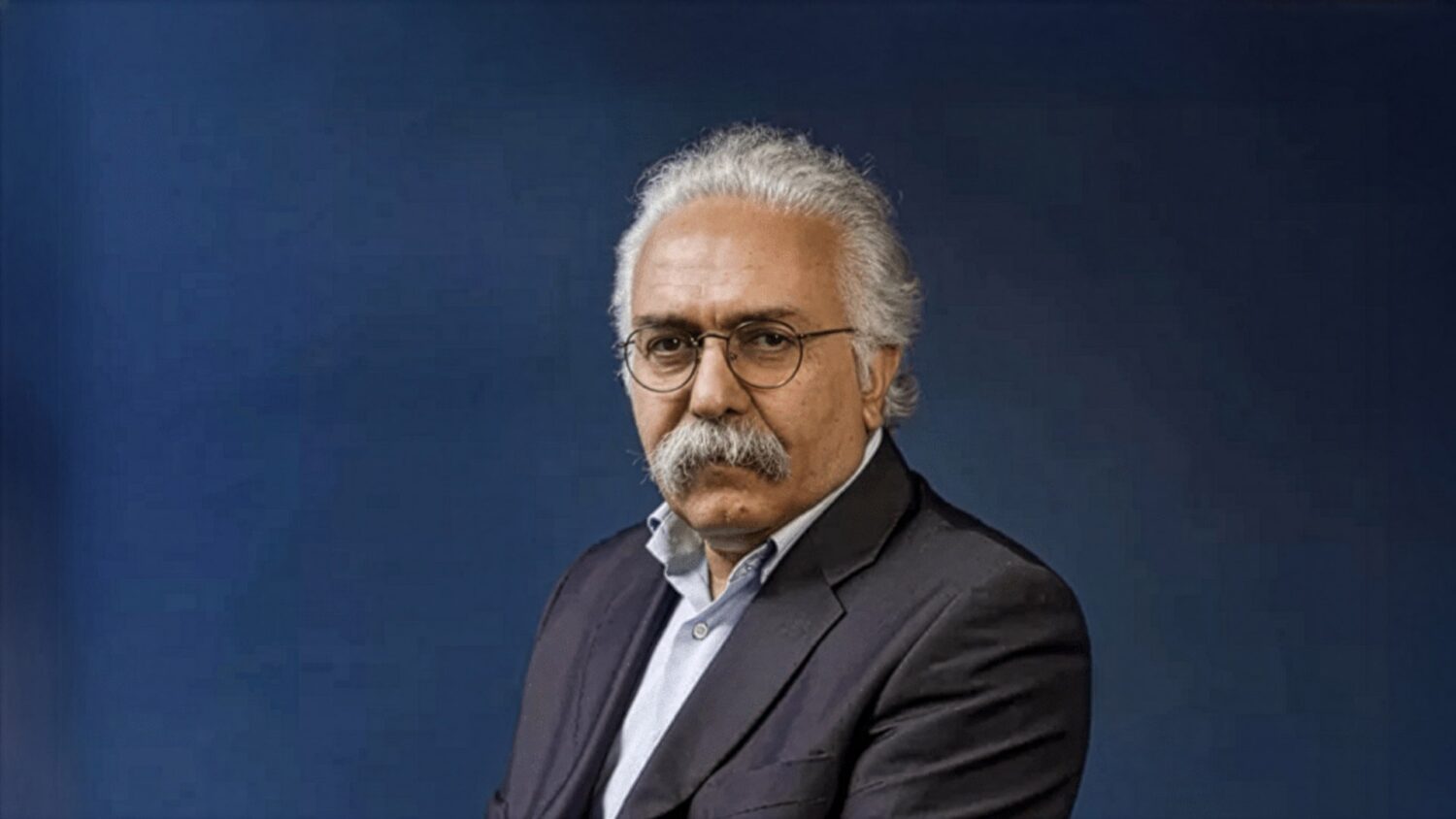 Professor Mohammad Amir Moezzi in a dark suit portrait, against dark blue background.
