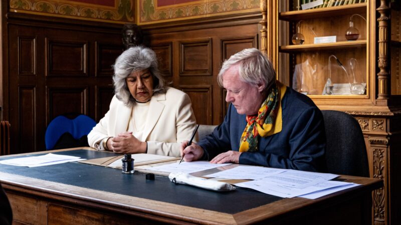 Two individuals signing documents at table - MoU.