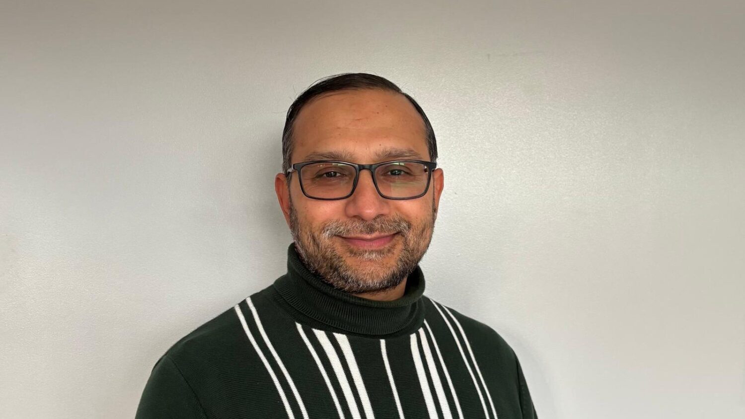 Kumail Rajani, Zahid Ali Fellow, wearing a striped sweater, standing against a white background.