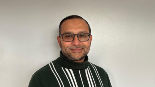 Kumail Rajani, Zahid Ali Fellow, wearing a striped sweater, standing against a white background.