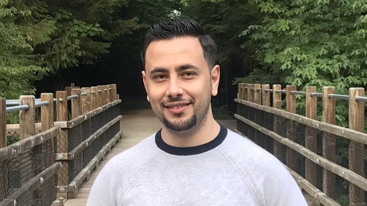 Rami Gargour stands on a wooden footbridge surrounded by trees, photographed outdoors in a natural setting.