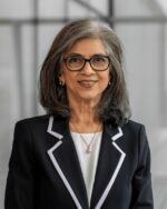 Minaz Fazal, IIS Governor, smiling in black-framed glasses and a black blazer with white-trimmed lapels.