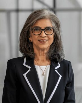 Minaz Fazal, IIS Governor, smiling in black-framed glasses and a black blazer with white-trimmed lapels.