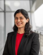 Professor Shenila Khoja-Moolji, IIS Governor, smiling in a black blazer over a red top.