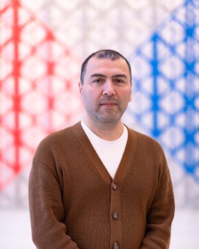 Muzaffar Zoolshoev in brown cardigan, against abstract background.