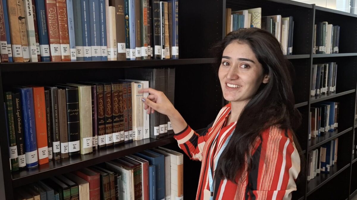 Farkhandah Jabeen selecting a book from Aga Khan Centre library shelves.