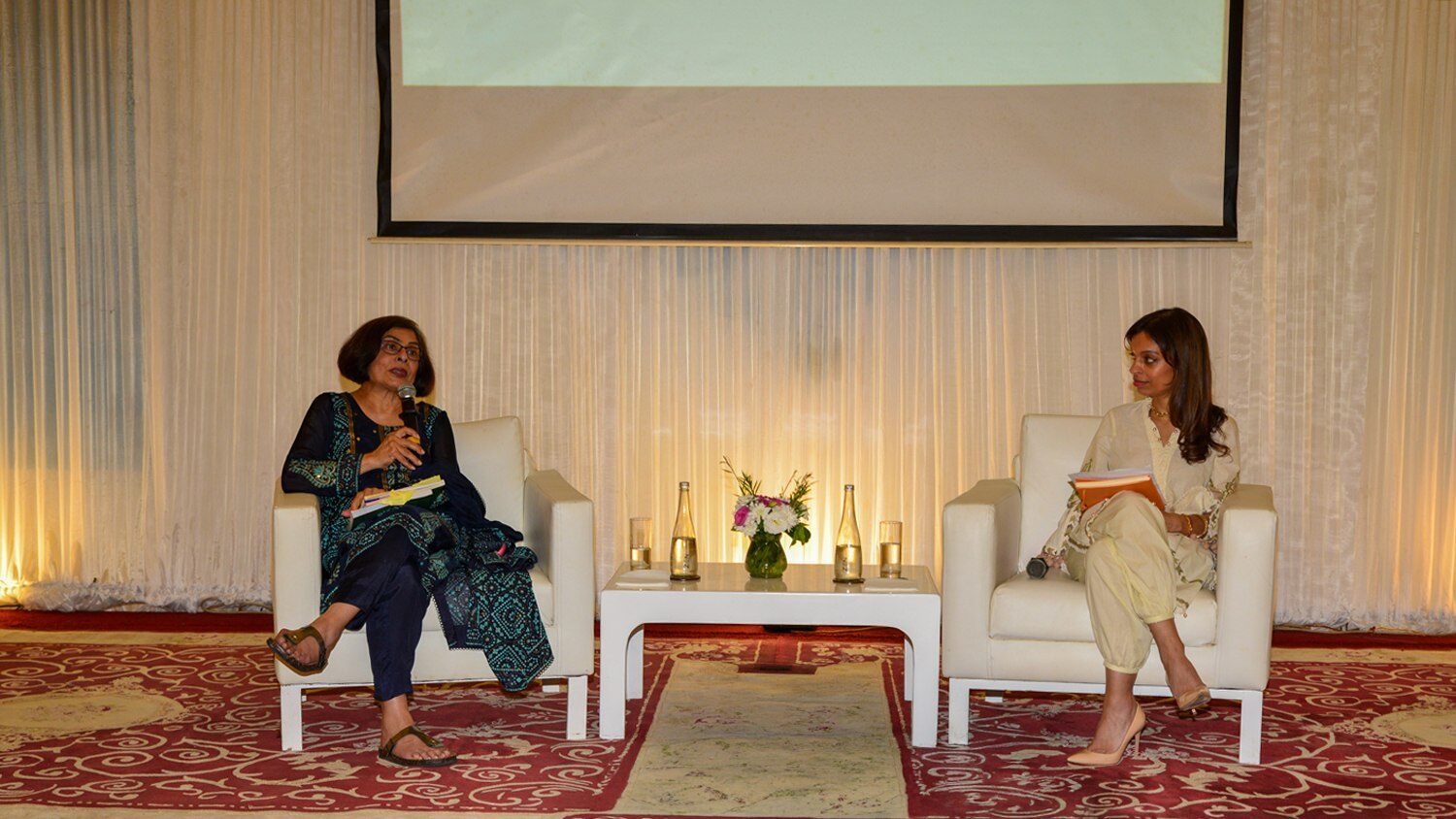 Dr Shainool Jiwa speaks into a microphone during a seated Book Talk discussion with Dr Fatima Dhanani in Dar es Salaam.