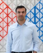 Hasan Ali Shah standing in front of a red and blue geometric lattice screen.