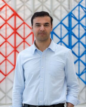 Hasan Ali Shah standing in front of a red and blue geometric lattice screen.