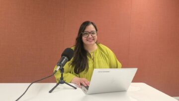 Naureen Ali seated at a table with a microphone and laptop, recording an episode of Voices of IIS