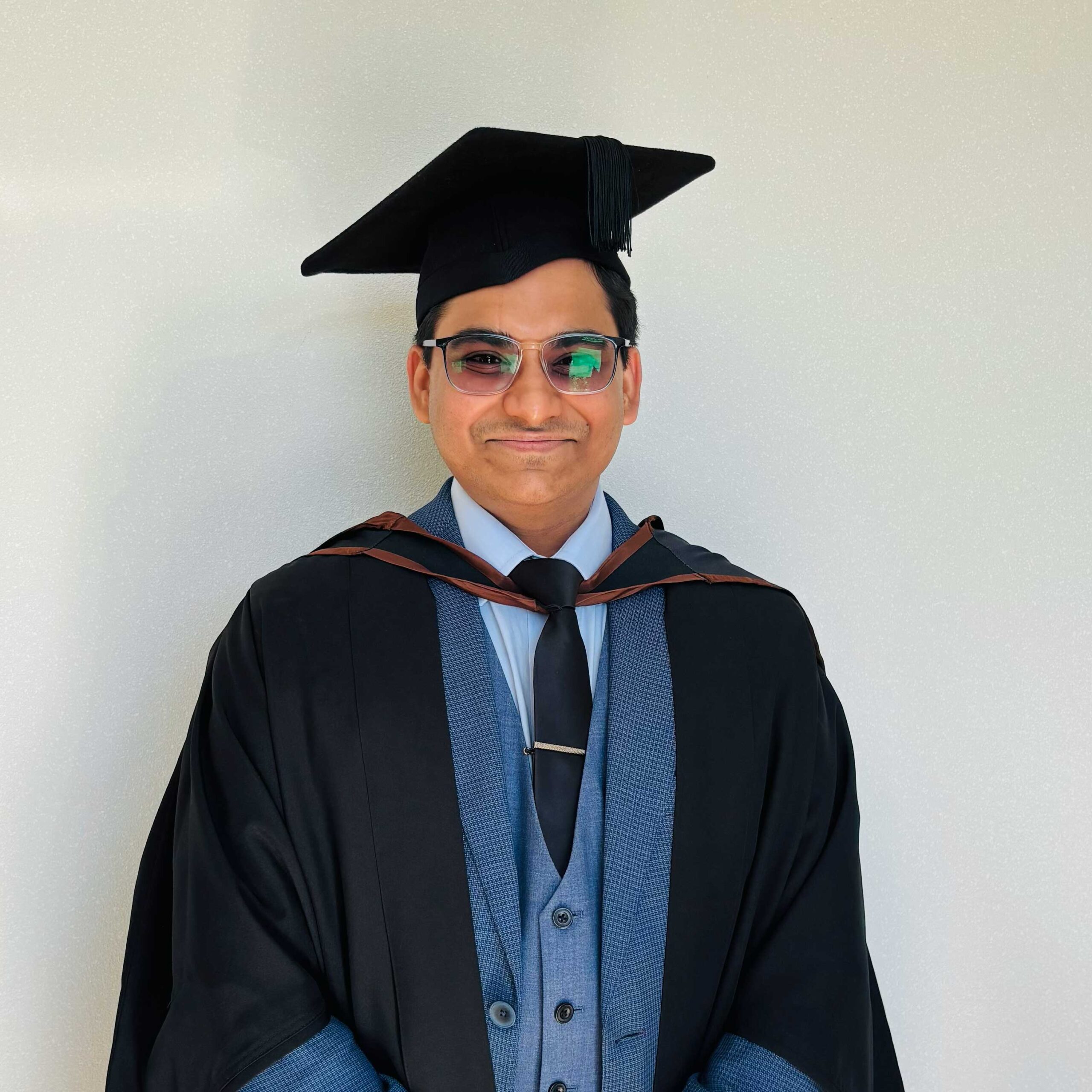 Muhammad Ali Sohail in academic cap and gown, standing against a plain wall.