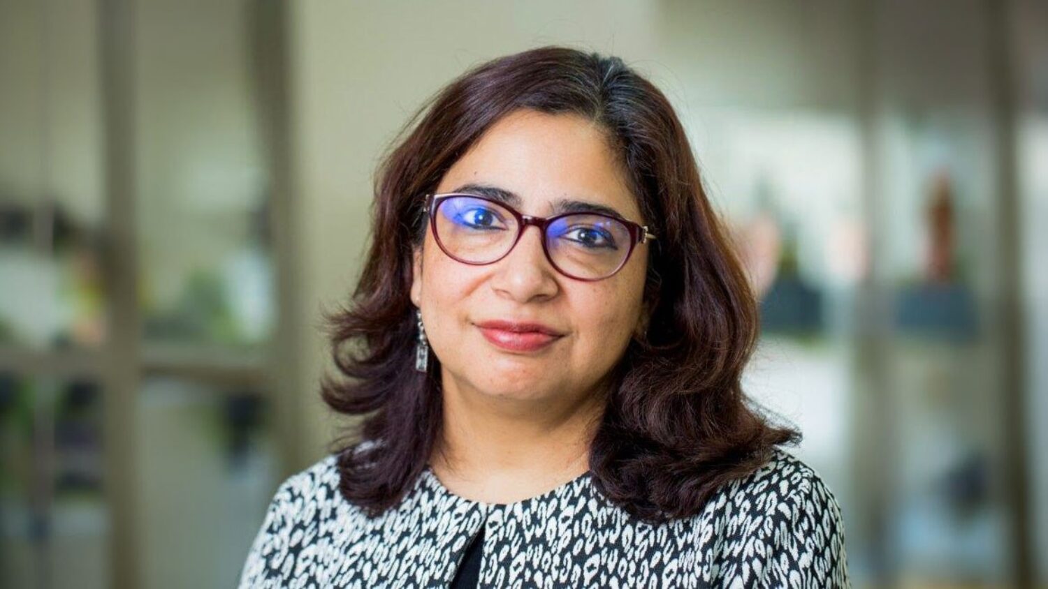 Professor Tashmin Khamis, head-and-shoulders portrait, wearing glasses and a patterned top.