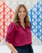 Launa Gauthier smiling in a magenta blouse in front of a red, grey and blue geometric lattice installation.