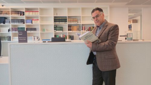 Dr Karim Javan reading his catalogue of Persian manuscripts beside a library reference desk.