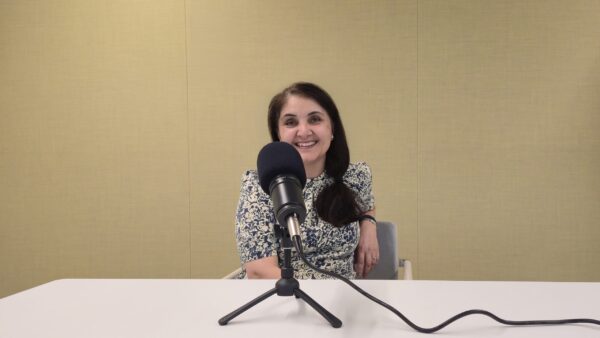 Dr Gurdofarid Miskinzoda smiling at a table behind a studio microphone during a Voices of IIS recording.