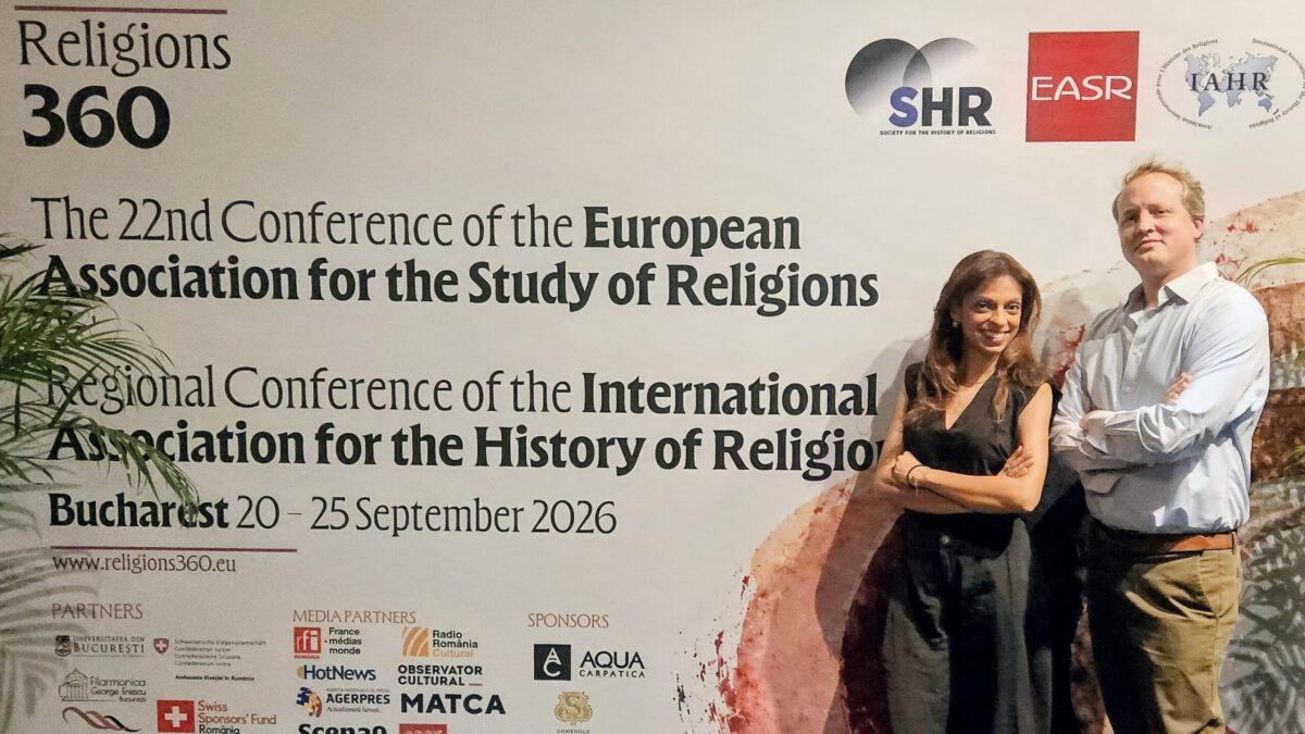 Dr Fatima Dhanani and Dr Alex Henley standing beside the Religions 360 congress banner in Bucharest.