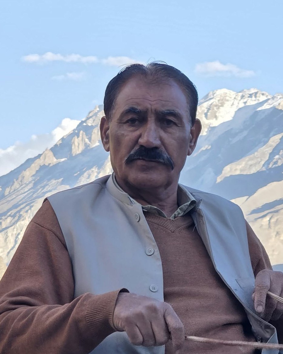 Ustad Baz, Hareep musician, holding drumsticks, with snow-capped mountains behind him.