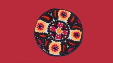 Embroidered cap seen from above, with orange and red floral medallions and paisley motifs on a white ground.