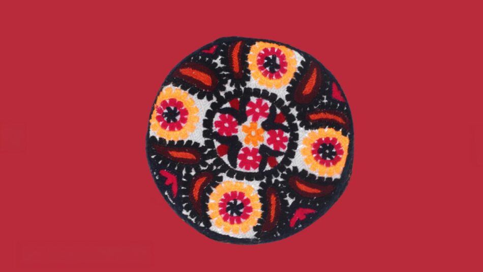 Embroidered cap seen from above, with orange and red floral medallions and paisley motifs on a white ground.
